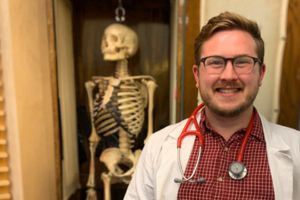 person smiling at camera w/skeleton in background