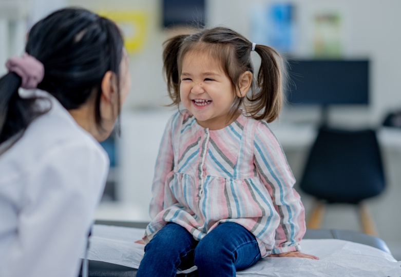 A young girl sits up on an exam table as she is looked over by her female doctor during an appointment.