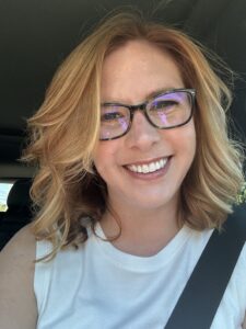 Person with light brown hair and glasses smiling at camera.