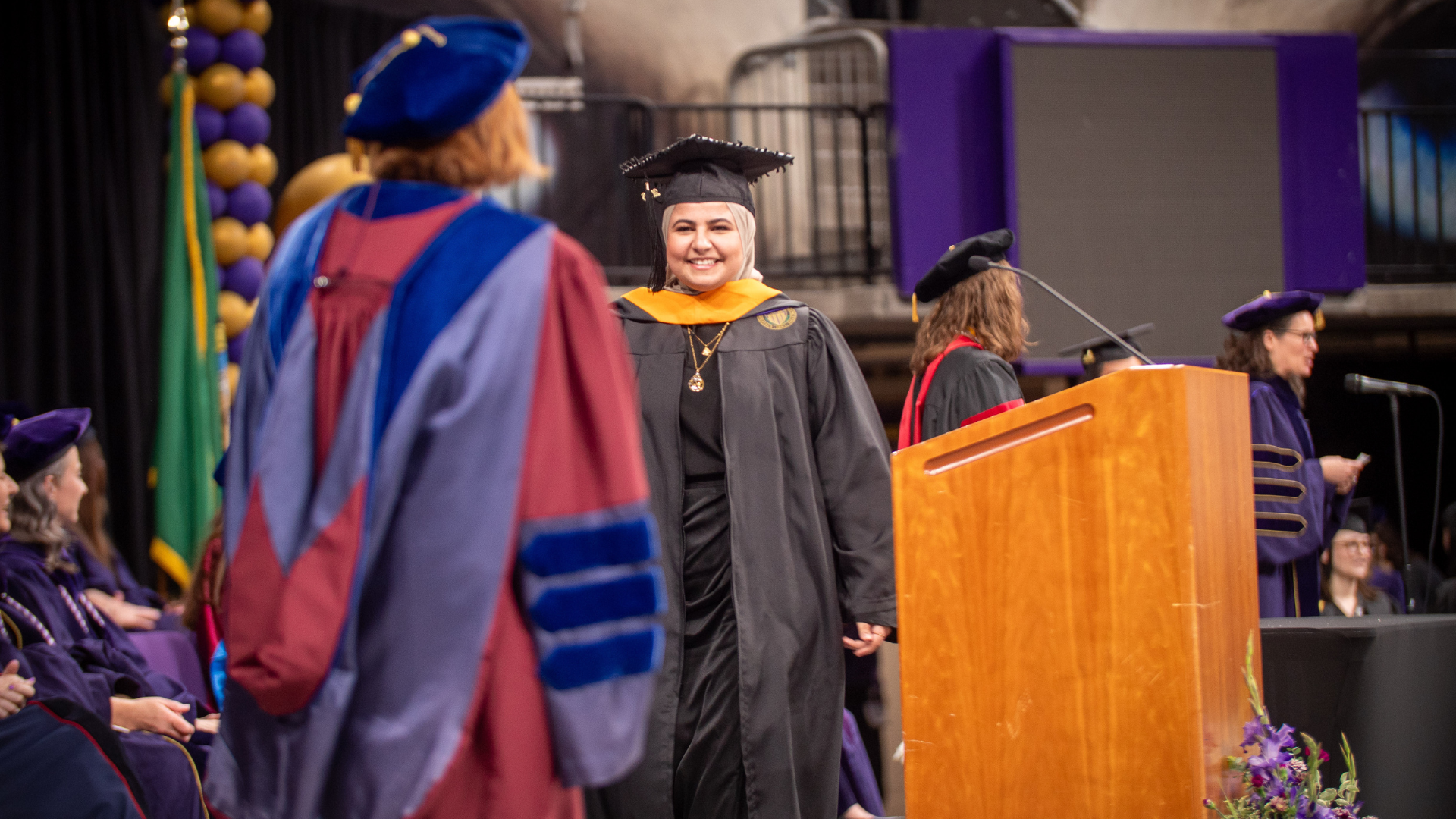 A graduation ceremony with a student walking across the stage and smiling.
