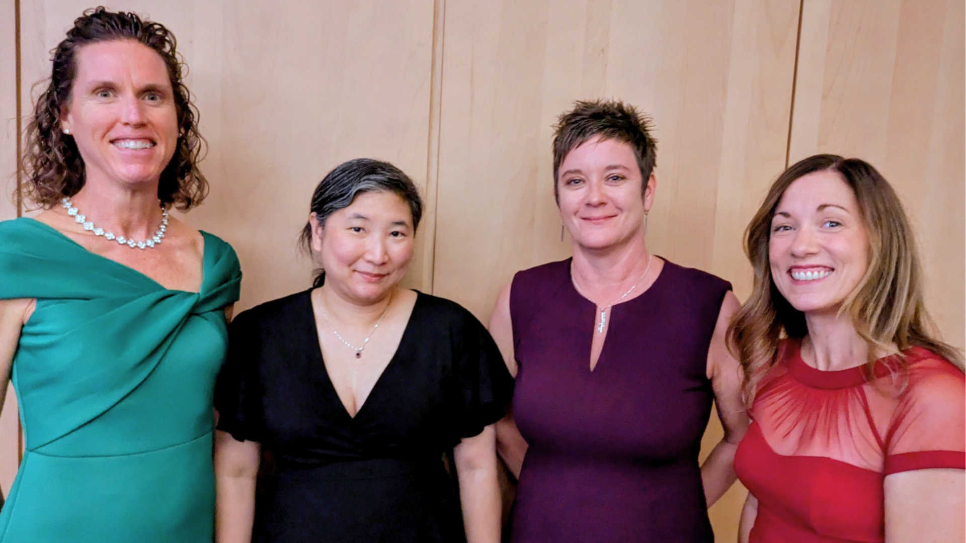 Four women standing in a row smiling at the camera.