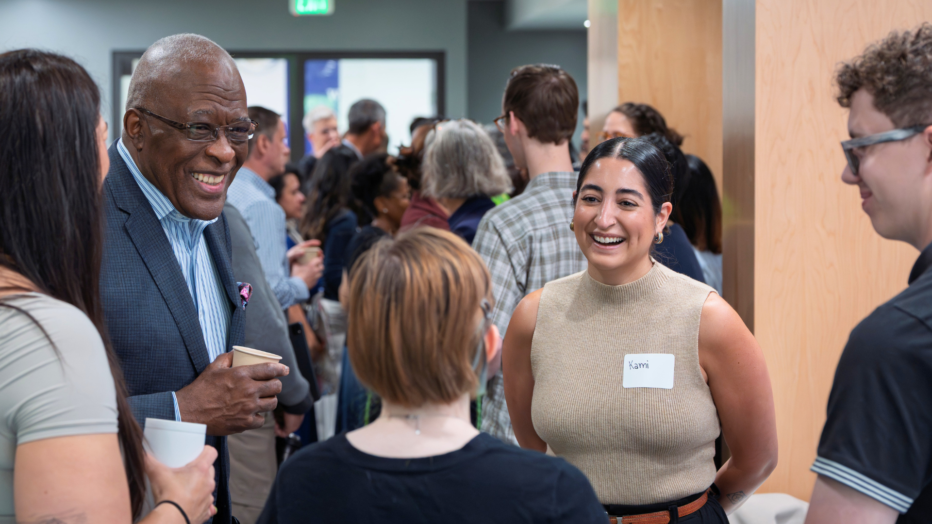 A group of people in a crowded room talking and smiling.