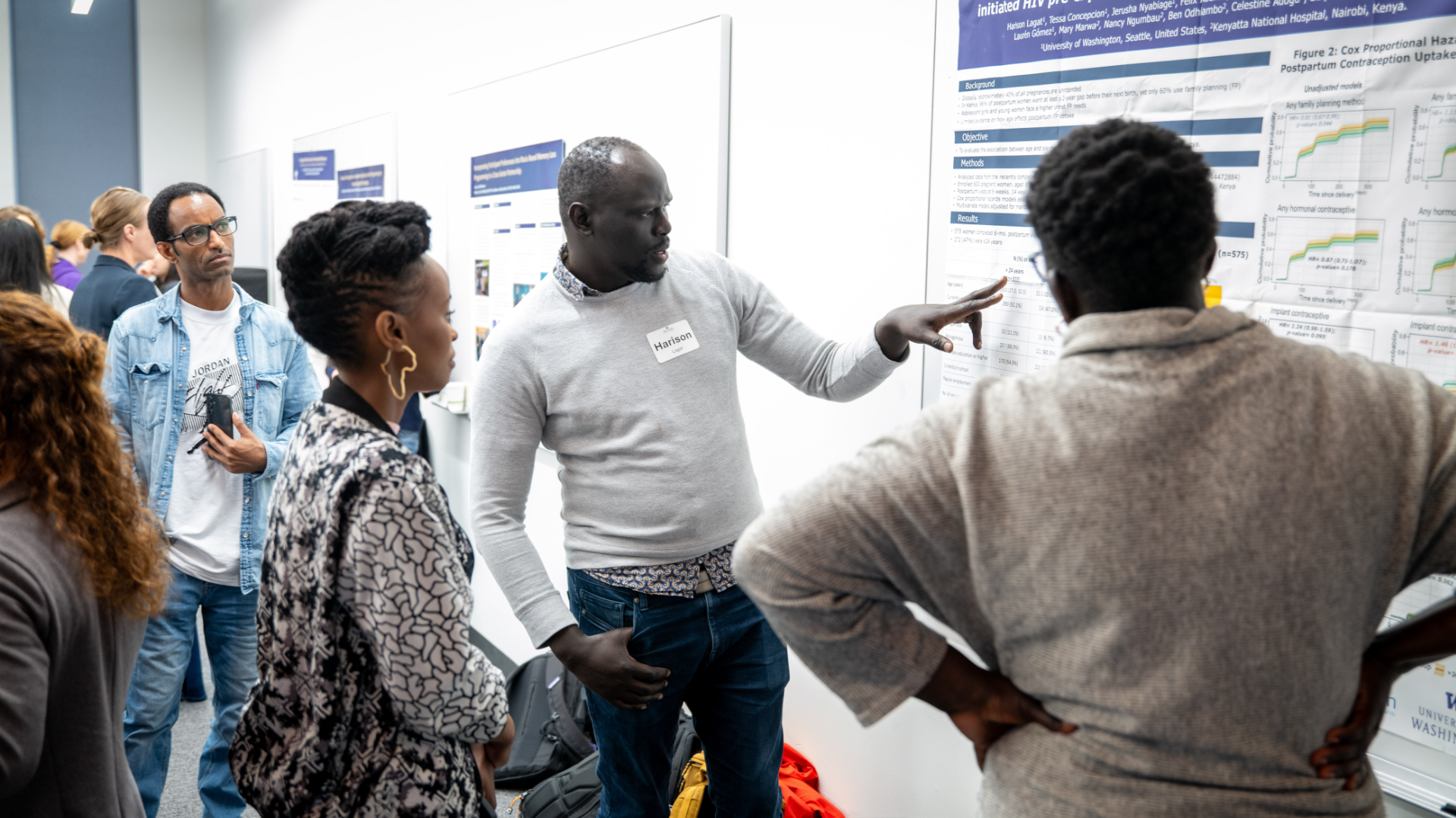 A man presenting his research to a crowd of people as he points to his research poster.