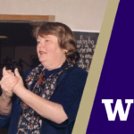 A woman in a blue patterned scarf and dark blue top stands indoors holding her hands together, with a purple-and-cream diagonal graphic and a large white letter “W” on the right.