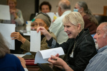 Seven attendees smile around a table covered with workshop materials, including papers, markers, cups and water bottles.